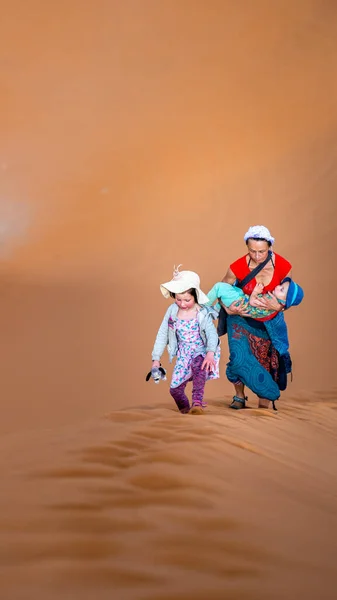 A mother with two children climbing a huge dune in the Sahara desert.