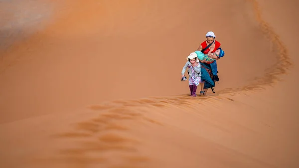 A mother with two children climbing a huge dune in the Sahara desert.