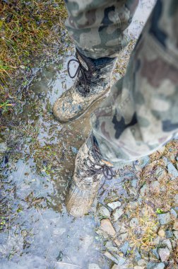 Close-up for a man's legs in military camouflage with a trekking wellington shoes dirty in mud.