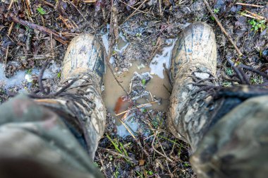 Close-up for a man's legs in military camouflage with a trekking wellington shoes dirty in mud.