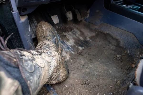 Close-up of a man\'s legs in military camouflage with trekking boots soiled in mud in the car