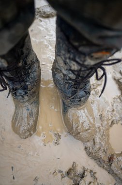 Close-up for a man's legs in military camouflage with a trekking wellington shoes dirty in mud.