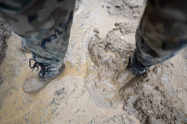 Close-up for a man\'s legs in military camouflage with a trekking wellington shoes dirty in mud.
