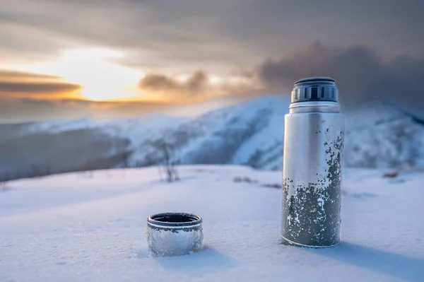 A thermos with a cup of coffee standing on an alpine meadow. Outdoor activity winter mountain landscape.