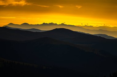Dağların karanlık siluetleri turuncu bir gökyüzünün arka planına karşı. Parang Dağları, Karpatlar ve Romanya 'dan görülen Fagaras Dağları.