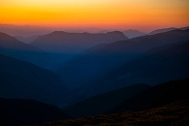 Güneş doğarken turuncu gökyüzü ile dağların karanlık siluetleri. Fotokopi alanı olan karanlık bir arkaplan. Parang Dağları, Romanya.