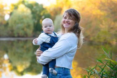 Genç ve güzel anne çocuğuyla dışarıda oynuyor. Denize karşı çocuğunu kucaklayan bir kadın. Anneler Günün kutlu olsun. Mutlu, güzel bir aile. Güzel sonbahar manzarası