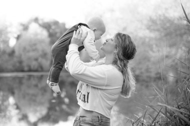 Genç ve güzel anne çocuğuyla dışarıda oynuyor. Denize karşı çocuğunu kucaklayan bir kadın. Anneler Günün kutlu olsun. Mutlu, güzel bir aile. Güzel sonbahar manzarası