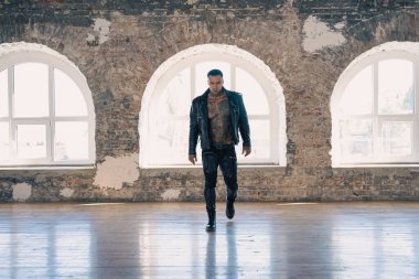 Büyük pencerenin önünde deri dövmeli seksi adam. Yakışıklı, genç, atletik erkek model. Çıplak gövdeli kaslı, seksi erkek. Dövmeli, acımasız, yakışıklı bir adam..