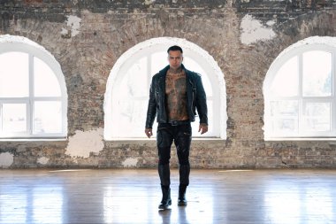 Büyük pencerenin önünde deri dövmeli seksi adam. Yakışıklı, genç, atletik erkek model. Çıplak gövdeli kaslı, seksi erkek. Dövmeli, acımasız, yakışıklı bir adam..