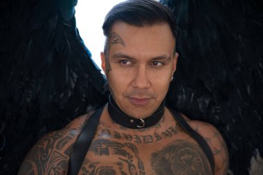 Erkek portresi. Yakışıklı erkek meleğin yakın portresi. Dövmeli adam. Deri giyen seksi adam. Tasmalı ve kırbaçlı bir adam. Koyu kanatlı açı