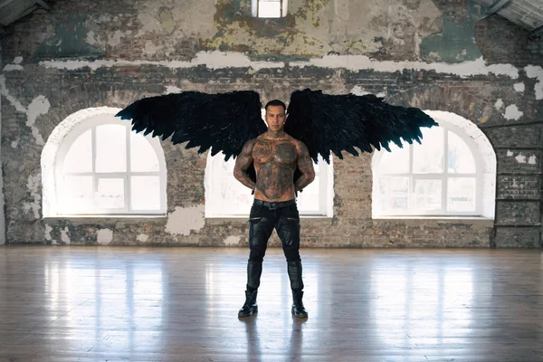 angel man with black wings, stand posing at camera. man fall from heaven, angel with muscular body gained freedom.  tattooed hot man. tattooed black angel. dark angel in leather