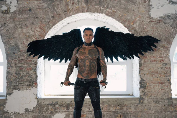 handsome man with wings.Male angel with black wings.  Muscular shirtless man with whip. Brutal handsome man with tattooed body. Muscular athletic sexy male