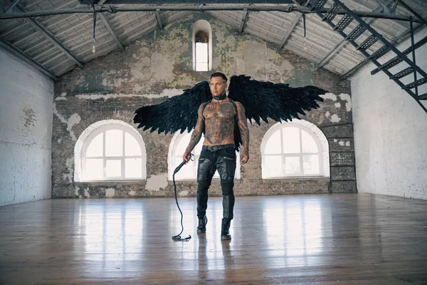 handsome man with wings.Male angel with black wings.  Muscular shirtless man with whip. Brutal handsome man with tattooed body. Muscular athletic sexy male
