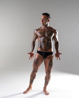 Genç yakışıklı vücut geliştirici poz veriyor, sporcu vücut geliştirme pozu veriyor. Güzel vücutlu seksi dövmeli adam stüdyoda kaslarını gösteriyor.