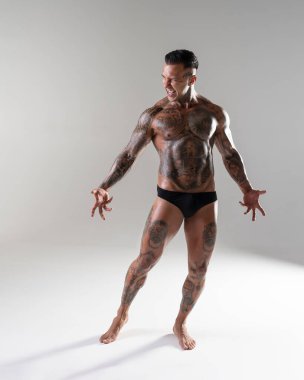 Genç yakışıklı vücut geliştirici poz veriyor, sporcu vücut geliştirme pozu veriyor. Güzel vücutlu seksi dövmeli adam stüdyoda kaslarını gösteriyor.