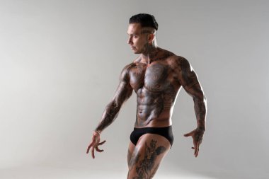 Genç yakışıklı vücut geliştirici poz veriyor, sporcu vücut geliştirme pozu veriyor. Güzel vücutlu seksi dövmeli adam stüdyoda kaslarını gösteriyor.