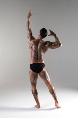 Genç yakışıklı vücut geliştirici poz veriyor, sporcu vücut geliştirme pozu veriyor. Güzel vücutlu seksi dövmeli adam stüdyoda kaslarını gösteriyor.