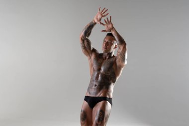 Genç yakışıklı vücut geliştirici poz veriyor, sporcu vücut geliştirme pozu veriyor. Güzel vücutlu seksi dövmeli adam stüdyoda kaslarını gösteriyor.