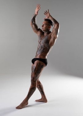 Genç yakışıklı vücut geliştirici poz veriyor, sporcu vücut geliştirme pozu veriyor. Güzel vücutlu seksi dövmeli adam stüdyoda kaslarını gösteriyor.