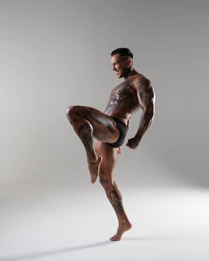 Güzel karın kasları olan genç kaslı adam. Hareketli bir dövüşçü. Dövmeli kickboksör. Dövüş sanatları eğitimi almış. Vücut geliştirme. Stüdyoda poz veren seksi bir adam.