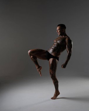 Güzel karın kasları olan genç kaslı adam. Hareketli bir dövüşçü. Dövmeli kickboksör. Dövüş sanatları eğitimi almış. Vücut geliştirme. Stüdyoda poz veren seksi bir adam.