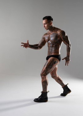 Genç yakışıklı vücut geliştirici poz veriyor, sporcu vücut geliştirme pozu veriyor. Güzel vücutlu seksi dövmeli adam stüdyoda kaslarını gösteriyor.