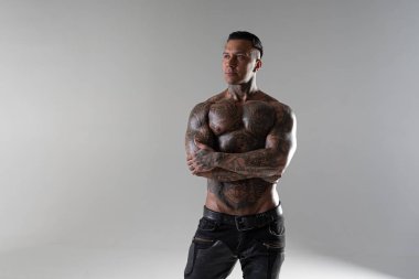 Genç yakışıklı vücut geliştirici poz veriyor, sporcu vücut geliştirme pozu veriyor. Güzel vücutlu seksi dövmeli adam stüdyoda kaslarını gösteriyor.