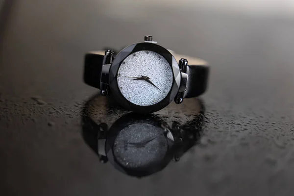 ブラックガラスのテーブルの手首の腕時計 スタイリッシュな時計 テーブルの上に水が落ちる 豪華な時計だ — ストック写真