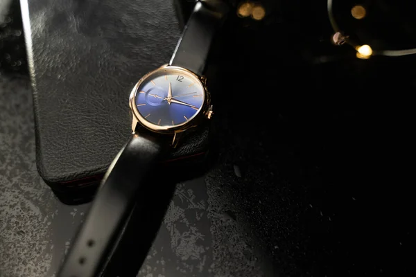 ブラックガラスのテーブルの手首の腕時計 スタイリッシュな時計 テーブルの上に水が落ちる 豪華な時計だ — ストック写真