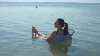 Gözlüklü güzel kız sahilde güneşleniyor. Suda bir kadın dolanıyor ve bir yerden izliyor. 