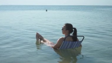 Gözlüklü güzel kız sahilde güneşleniyor. Suda bir kadın dolanıyor ve bir yerden izliyor. 