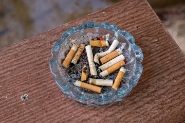 Yemek masasındaki kül tablasında büyük miktarda sigara izmariti, sigara içerken oluşan akciğer kanserinin tehlikelerini gösteren bir resim..