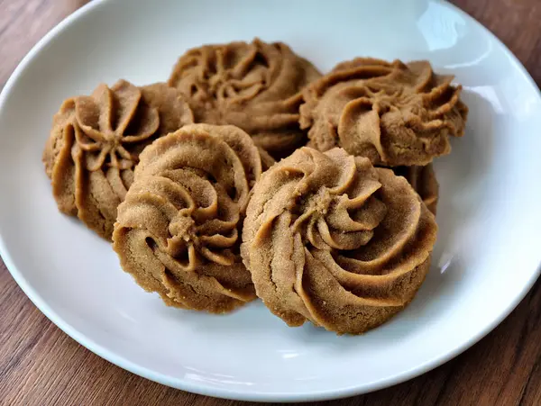 Sabahları beyaz tabakta kahve aromalı lezzetli kurabiyeler ve sıcak kahve ile servis edilen ahşap bir masa..