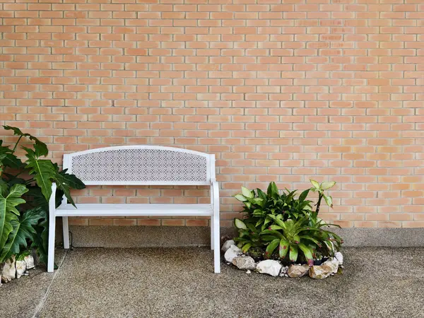 Rahatlamak için tuğla duvarlı binanın önüne temiz, beyaz bir metal bank konur..