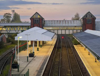 İngiltere 'nin Kuzey Galler kentindeki Wrexham şehrinde, alacakaranlıkta tren istasyonunun platformlarının ve raylarının açılı görüntüsü.