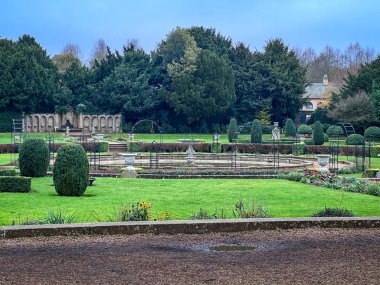 Düzgün kesilmiş çalıları ve göleti olan resmi bir bahçe.