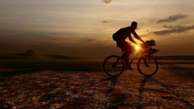 Sahada bisiklet süren bir adamın silüeti.