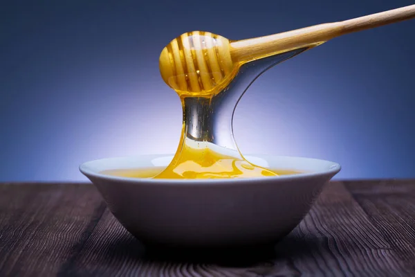 honey drips from the spoon into a white bowl with a blue background