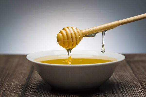 honey drips from the spoon into a white bowl still life