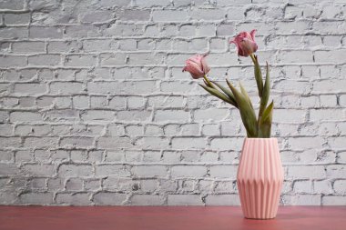 Pink Tulips in Vase on Pink Table Behind a brick Wall,copy space