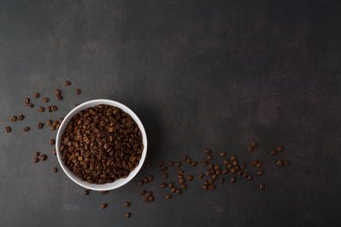 Beyaz kasede kahve çekirdekleri. Üst Manzara. Karanlık taş arka planda. Boşluğu kopyala