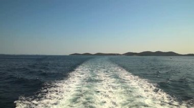 Uyanış kuyruğunun yavaş çekim görüntüsü denizdeki büyük bir yolcu gemisinin arkasında. Arka planda güzel dağlar