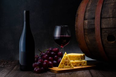 Eski ahşap masada bir bardak kırmızı şarap, peynir ve üzüm. koyu arkaplan.
