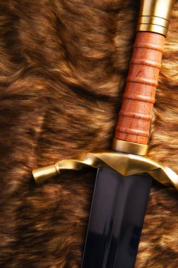 Parlak bir bıçakla, kahverengi ve siyah renkli hayvan kürkünün üzerine yerleştirilmiş bir kılıcın yakın çekimi..