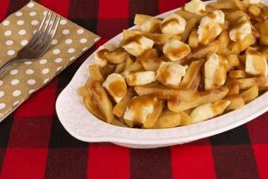 Poutine plaka üzerinde kırmızı ve siyah tartan masa örtüsü. Yemek patates kızartması, sığır eti sos ve lor peyniri ile pişmiş. Kanada mutfağı.