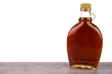 Zengin altın akçaağaç şurubuyla dolu cam şişe, beyaz arka planda taştan bir yüzeye yerleştirilmiş. Yemek fotoğrafçılığı, reklamcılık ya da kahvaltı ve doğal tatlandırıcı kavramları için mükemmel..