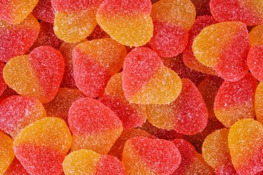 Renkli, şeker kaplı, kalp şeklinde şekerler, canlı kırmızı ve sarı tonlarda. Tatlı, çiğnenmiş doku, Sevgililer Günü tasarımları ve kutlamaları için mükemmel bir şenlik ve romantik arka plan oluşturuyor..