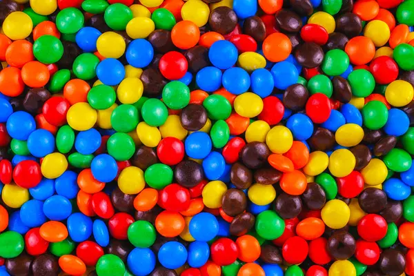 Canlı ve neşeli bir yığının içinde renkli çikolata kaplı çikolatalar. Parlak kırmızı, mavi, sarı, yeşil ve turuncu tatlılar partiler, tasarımlar ve reklamlar için mükemmel neşeli, şenlikli bir zemin oluşturur..