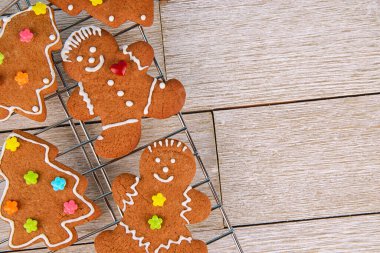 Taze pişmiş zencefilli çörekler ve Noel ağacı kurabiyeleri kremalı ve renkli parçacıklar kırsal bir ahşabın üzerinde soğutuluyor, sıcak, bayram pişirme atmosferi yaratıyor..